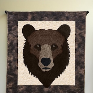 May include: A brown bear face quilt with a brown and white background. The quilt is hanging on a wall. The text "Example of what can be made." is below the quilt.