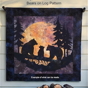 Pode incluir: Uma colcha com fundo azul escuro e uma grande lua laranja no centro. Três silhuetas de ursos negros estão em um galho na frente da lua. A colcha é intitulada "Spindles and Quilts Bears on Log Pattern" e diz "Exemplo do que pode ser feito."