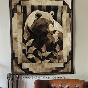 Puede incluir: Un edredón de pared rectangular que presenta un gráfico central de una cabeza de oso en tonos marrón, bronceado y crema. El diseño incluye motivos de hojas estilizadas en la parte inferior y un borde geométrico. El texto "Example of what can be made" es visible.