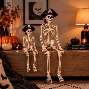 May include: Two off-white plastic skeleton figures in a seated position, each wearing a black pirate hat with a white skull and crossbones emblem. The skeletons feature articulated joints, realistic rib cages, and detailed skulls with hollow eye sockets.