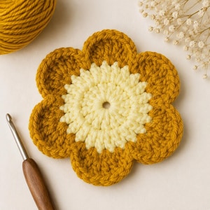 May include: A crocheted flower coaster featuring a central cream-colored circular section surrounded by six rounded mustard-yellow petals. The item is crafted with visible yarn stitches and is positioned next to a wooden crochet hook and yarn.