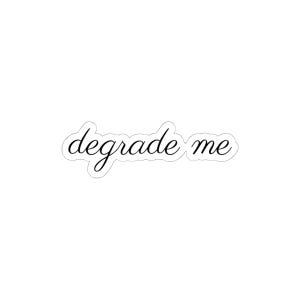 May include: A die-cut sticker featuring the text "degrade me" written in a black, flowing cursive script font. The sticker has a thin white border that follows the contour of the lettering, creating a clean and distinct outline for the design.