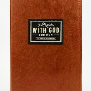 Könnte beinhalten: Ein rechteckiges Buch mit einem strukturierten, braunen, lederartigen Einband. Mittig auf der Vorderseite befindet sich ein schwarzes rechteckiges Etikett mit weißem Text: One Minute WITH GOD FOR MEN 365 DAILY DEVOTIONS. Das Buch hat genähte Kanten.