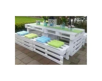 Puede incluir: Una mesa y dos bancos a juego hechos de palés de madera blanca. La mesa cuenta con un camino de mesa verde claro, un farol blanco y pequeños jarrones. Los bancos están cubiertos con cojines cuadrados en azul claro, verde lima y verde brillante.