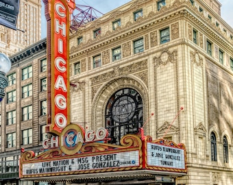 May include: Exterior view of the Chicago Theatre, a historic landmark with a large marquee. The marquee displays the text "CHICAGO" in illuminated letters, with the show's name and performers listed below. The building's facade is ornate.