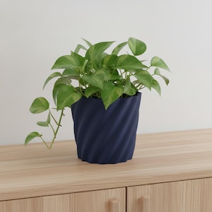 Peut inclure: Une plante pothos au feuillage vert vif en forme de cœur, installée dans un pot bleu marine profond. Le pot présente une texture verticale en spirale ou torsadée sur toute sa surface extérieure, offrant un contraste avec les feuilles.