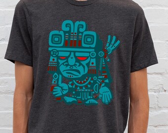 May include: A dark grey t-shirt with a teal and red graphic print of a stylized Mayan deity with a fierce expression.