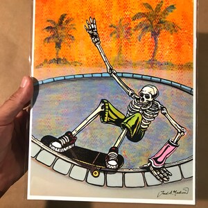 Pu&ograve; includere: Uno scheletro con pantaloncini verdi e gomitiere rosa sta facendo skateboard in una piscina. La piscina &egrave; circondata da un bordo di piastrelle blu e bianche. Lo sfondo &egrave; un tramonto con palme.
