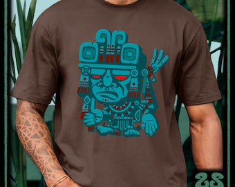 May include: A brown short-sleeved t-shirt featuring a large graphic print of a stylized turquoise and red figure with an ornate headdress and glowing red eyes. The design is centered on the chest, showcasing intricate geometric patterns and lines.
