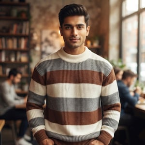 May include: A long-sleeve knit sweater featuring horizontal stripes in alternating colors of cream, medium brown, and heather gray. The garment has a ribbed crew neckline, ribbed cuffs, and a ribbed hem, constructed with a thick, textured yarn.