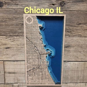 May include: A rectangular wooden wall art piece featuring a layered 3D bathymetric map of Chicago, IL. The left side shows a detailed street grid, while the right side depicts the blue depths of Lake Michigan. The text Chicago IL is visible.