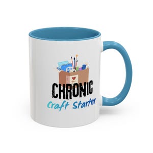 May include: A white ceramic mug with a blue interior and handle. The front features a graphic of a brown box filled with art supplies, including brushes and paint. Below the box, the text reads CHRONIC in black and Craft Starter in blue.
