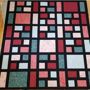 Puede incluir: Una colcha con un patrón geométrico de cuadrados y rectángulos rojos, rosados, verdes y blancos sobre un fondo negro.