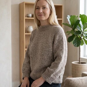 Può includere: Un maglione in maglia color beige mélange a maniche lunghe, caratterizzato da un collo alto a coste, polsini a coste e orlo a coste. Il maglione è realizzato con un filato testurizzato e maculato, con una vestibilità ampia e spalle scese.