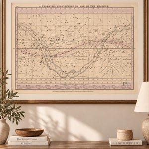 Könnte beinhalten: Eine gerahmte, vintage-artige Himmelskarte mit dem Titel A CELESTIAL PLANISPHERE, OR MAP OF THE HEAVENS. Der Druck zeigt einen beigen Hintergrund mit schwarzen Sternkarten, Sternbildnamen und einem rosa horizontalen Band in der Mitte.