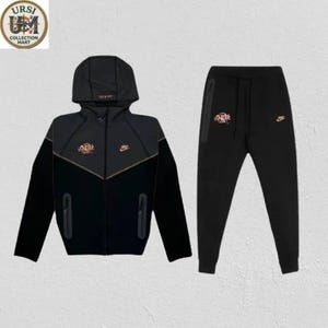 May include: A black Nike Tech Fleece tracksuit consisting of a hooded zip-up jacket and matching joggers. The jacket features a dark grey chest panel, two zippered side pockets, and a small Nike logo. The joggers include a side zip pocket.