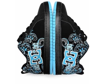 May include: A pair of black sneakers featuring a light blue DC logo on the side, accented with intricate white and light blue swirling patterns. The shoes have black laces, a black midsole, and a light blue outsole, presented side by side.
