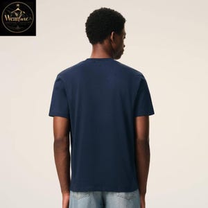 May include: A solid navy blue short-sleeved t-shirt with a crew neckline, shown from the back. The garment features a plain, unpatterned design with a standard fit, paired with light blue denim jeans that have visible back pockets and stitching.