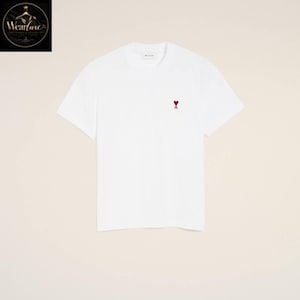 May include: A plain white short-sleeved t-shirt featuring a small, embroidered red heart logo with a cross symbol centered on the upper left chest area. The garment has a classic crew neckline and a clean, solid white fabric construction throughout.
