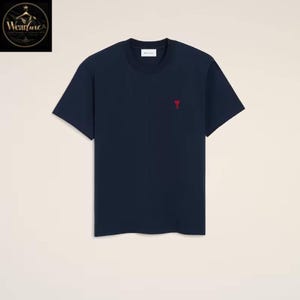May include: A navy blue short-sleeved t-shirt featuring a crew neckline and a small red heart-shaped logo embroidered on the left chest area. The garment includes a white interior neck label with black text, presented against a plain background.