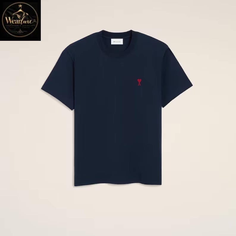 May include: A navy blue short-sleeved t-shirt featuring a crew neckline and a small red heart-shaped logo embroidered on the left chest area. The garment includes a white interior neck label with black text, presented against a plain background.