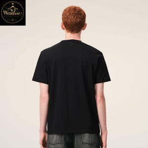 May include: A plain black short-sleeved t-shirt with a crew neckline, shown from the back. The shirt is worn with dark grey denim jeans. The fabric appears smooth and solid black, featuring a simple, standard cut with short sleeves and a round neck.
