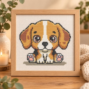 Può includere: Un ricamo a punto croce incorniciato raffigurante un cucciolo in stile cartoon con grandi occhi scuri, pelo marrone chiaro e bianco e cuscinetti delle zampe rosa. Il cucciolo è centrato su un tessuto a griglia bianco in una cornice di legno.