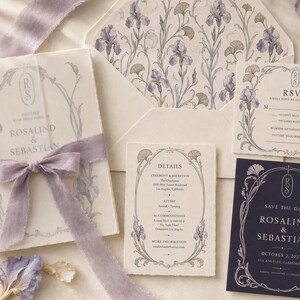 May include: A wedding stationery set featuring cream and dark navy cards with purple iris illustrations. The set includes an invitation tied with a lavender silk ribbon, an RSVP card, a details card, and a save the date card with floral borders.
