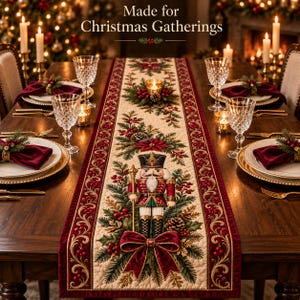 May include: A rectangular table runner featuring a central nutcracker illustration, pine branches, red berries, and pinecones on a cream background, bordered by deep red velvet fabric with gold scrollwork. Text reads: Made for Christmas Gatherings.
