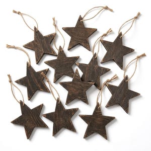 May include: A collection of twelve dark brown wooden star ornaments, each featuring a visible wood grain texture and a thin, light brown jute twine loop attached to the top point for hanging purposes.