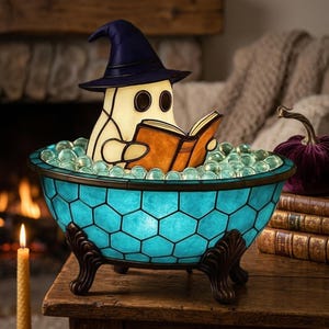 Könnte beinhalten: Eine dekorative Lampe in Form einer Badewanne mit Klauenfüßen und blauem Wabenmuster, gefüllt mit klaren Glaskugeln. Eine cremefarbene Geisterfigur mit einem dunkelblauen spitzen Hut sitzt in der Wanne und hält ein offenes braunes Buch.
