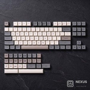 May include: A mechanical keyboard keycap set featuring a mix of light beige and dark gray keys. The layout includes standard alphanumeric keys, function keys, and a numeric cluster. Several keys display unique icons like an eye and rocket.