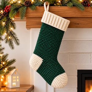 May include: A crochet Christmas stocking featuring a deep forest green body with a contrasting cream-colored ribbed cuff, heel, and toe. The stocking includes a small matching cream loop at the top for hanging, showcasing a textured yarn construction.