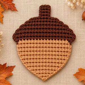 May include: A crocheted acorn-shaped coaster featuring a dark brown cap and a light tan base. The item is crafted with a dense, uniform stitch pattern, creating a flat, textured surface that mimics the appearance of a natural acorn.