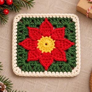 May include: A square crochet coaster featuring a central yellow flower surrounded by red petals, set against a dark green background. The square is bordered by a thick cream-colored crochet edge, creating a distinct floral pattern in the center.