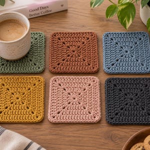May include: A set of six square crochet coasters in various solid colors including sage green, terracotta, dusty blue, mustard yellow, blush pink, and charcoal gray. Each coaster features a central square pattern with visible yarn stitching.