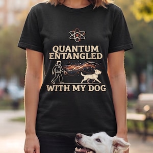Könnte beinhalten: Ein schwarzes kurzärmeliges T-Shirt mit einem Grafikdruck eines Atomsymbols über dem Text "QUANTUM ENTANGLED WITH MY DOG". Das Design zeigt eine Strichzeichnung einer Person, die einen Hund ausführt, verbunden durch eine leuchtende, wellenförmige Linie.