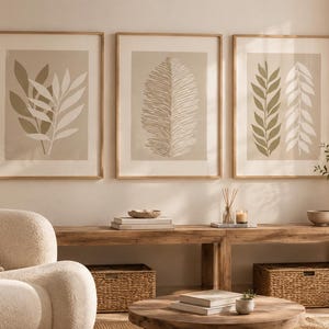 Könnte beinhalten: Drei gerahmte Wandbilder mit botanischen Illustrationen von Blättern in Beige-, Creme- und Salbeigrüntönen. Jeder Druck ist in einen hellen Holzrahmen gefasst und zeigt eine neutrale Farbpalette mit organischen Blattmustern.