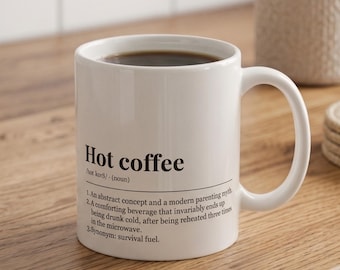 May include: A white ceramic mug filled with dark coffee, featuring black printed text that reads: Hot coffee /hɒt kɔːfi/ (noun) 1. An abstract concept and a modern parenting myth. 2. A comforting beverage that invariably ends up being drunk cold.
