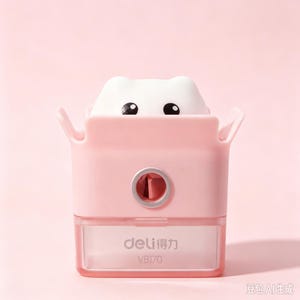 May include: A pink pencil sharpener featuring a white cat-shaped top with black eyes. The sharpener has a clear plastic shavings container at the bottom with the text deli and VB170 printed on the front. The design includes two small ears.