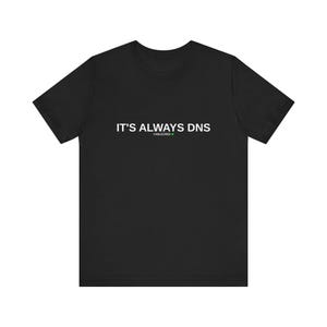 Könnte beinhalten: Ein schwarzes Kurzarm-T-Shirt mit dem weißen Schriftzug "IT'S ALWAYS DNS" auf der Brust. Unter dem Haupttext erscheint das Wort "CABLECRED" in einer kleineren Schriftgröße, begleitet von einem kleinen grünen Kreissymbol.