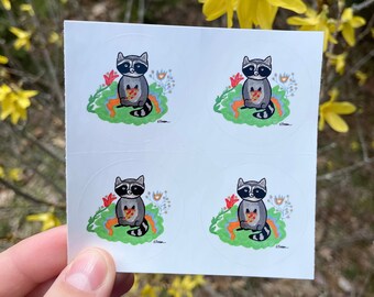 May include: Four round stickers featuring a cartoon raccoon holding a slice of pizza. The raccoon is sitting on a bed of green grass with colorful flowers. The stickers are white with a black outline.