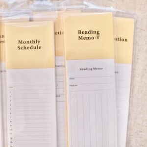 May include: A set of vertical paper planners and memo pads in clear plastic sleeves. The pads feature pale yellow headers with black text reading Monthly Schedule and Reading Memo-T, with white lined sections for notes and dates below.