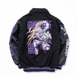 Könnte beinhalten: Eine schwarze Collegejacke mit einer großen Stickerei auf der Rückseite, die eine Figur mit Blitzen, den Text SUN GOD NIKA und BLACKSEVEN zeigt. Die Ärmel sind schwarz und mit weißen sowie violetten Logos und Symbolen an den Schultern bestickt.