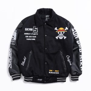 May include: A black varsity jacket featuring white embroidered text including Gear 5, Monkey D. Luffy, Sun God Nika, and Transform. The front displays a skull and crossbones logo with a straw hat. The sleeves have white text and graphics.