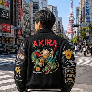 May include: A black varsity jacket featuring embroidered Dragon Ball graphics on the back and sleeves. The back displays a character riding a green dragon with the text AKIRA and Toriyama. The sleeves feature additional character art and text.