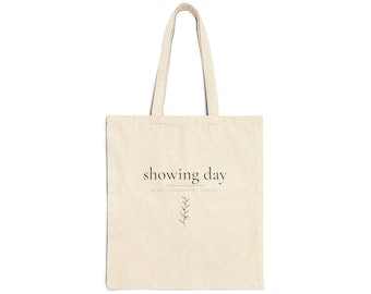 May include: A beige canvas tote bag with two shoulder straps. The front features the black text "showing day" above a horizontal line, the words "KEYS CONTRACTS COFFEE" in smaller font, and a small, simple line drawing of a leafy plant stem.