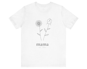 May include: A white short-sleeve t-shirt featuring a black line art graphic of two flowers. Below the flowers, the word "mama" is printed in a serif font, with the names "AVA" and "NOAH" positioned underneath separated by a horizontal line.