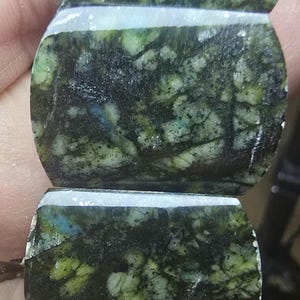 May include: A bracelet composed of polished, rectangular stone beads featuring a mottled pattern of deep forest green, black, and occasional white veins. The stones have a smooth, glossy finish and are strung together in a linear arrangement.