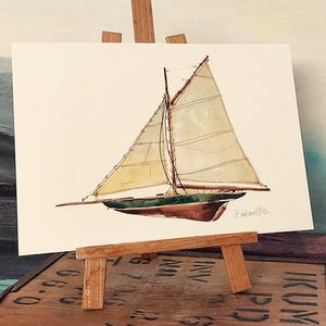 Pode incluir: Pintura em aquarela de um veleiro com velas bege, convés verde e casco marrom. A obra de arte é exibida em um pequeno cavalete de madeira. A assinatura do artista é visível no canto inferior direito.